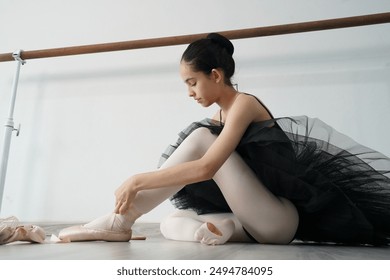 Fourteen-year-old teenage girl in a black ballet dress and ballet shoes with ribbons is practicing ballet in a studio. - Powered by Shutterstock