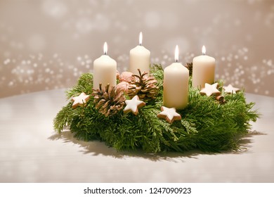 Fourth  Advent - decorated Advent wreath from evergreen branches with white burning candles, tradition in the time before Christmas, warm background with festive bokeh and copy space, selected focus