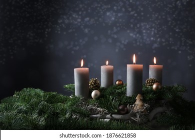 Fourth advent with four burning candles on fir branches with Christmas decoration against a dark grey background, copy space, selected focus, narrow depth of field
