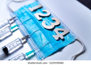 Fourth covid vaccine shot and jab concept with face mask. Four syringes are seen on table as a concept for the 4th covid-19 vaccine dose, also called booster shot, to fight the covid omicron varian - Shutterstock ID 2129190440