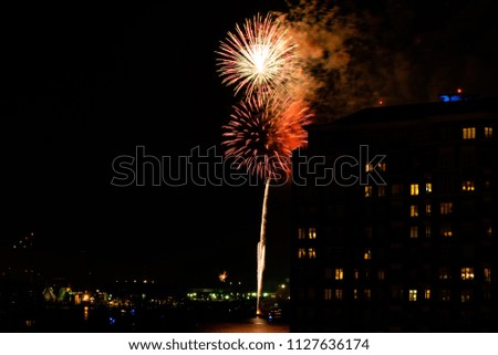 A Fourth of July fireworks display explodes over the waterfront in the city center of Norfolk Virginia, in the context of buildings, apartments, and dwellings