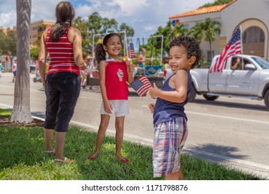 Fourth of July parade passes by as the kids enjoy waving the American flag with Mom. Toddler shows his swag holding the American flag.