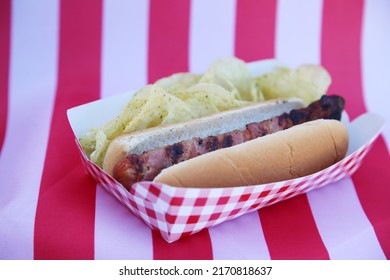 Fourth Of July Party HOT DOG. Fresh Cooked Hot Dog In A Bun. Fresh Cooked HOT Dog With Chips On An American Flag. 4th Of July BBQ Party. Party Food. Independence Day Hot Dog. Lunch. Dinner. Snack.