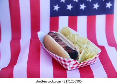 Fourth Of July Party HOT DOG. Fresh Cooked Hot Dog In A Bun. Fresh Cooked HOT Dog With Chips On An American Flag. 4th Of July BBQ Party. Party Food. Independence Day Hot Dog. Lunch. Dinner. Snack.