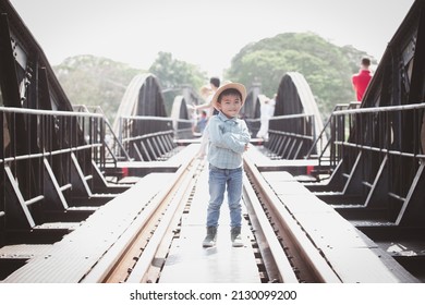 A four-year-old boy in a hat, a plaid shirt, jeans, crossed his arms and smiling charmingly on the railroad tracks. as people pass by 