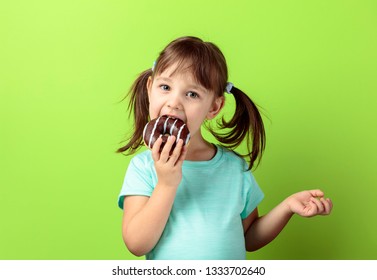 Four-year-old girl in a turquoise t-shirt eat donut. The girl's hair is tied in tails. green background.