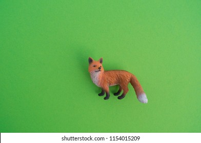 An fox animal is a children's toy. Plastic figurine for the game. Green background. Farm and the zoo.