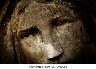 Fragment of antique statue of crying Virgin Mary. Tears on her face as symbol of pain, death and resurrection of Jesus Christ. Fragment of an ancient statue. Horizontal image.