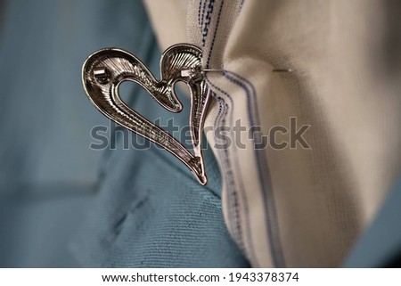 a fragment of a blue denim jacket and a scarf with an unbuttoned metal brooch in the shape of a heart