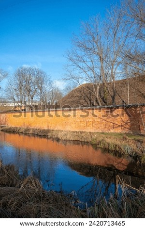 Fragment of a brick wall surrounding a military fortress from tsarist times, forest, water in the moat
