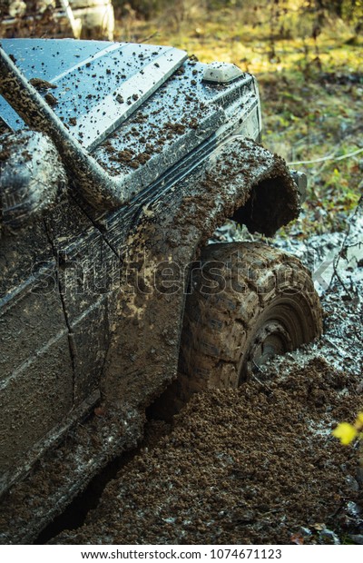 Fragment of car stuck\
in dirt, close up. Dangerous expedition concept. Offroad tire\
covered with mud on nature background. Wheel in deep puddle of mud\
overcomes obstacles.