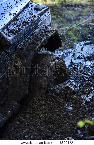 Fragment of car stuck in\
dirt, close up. Offroad tire covered with mud on nature background.\
Wheel in deep puddle of mud overcomes obstacles. Impassibility of\
roads concept.