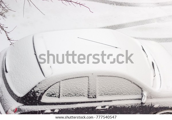 Fragment of car top\
with roof, side windows, rear window and windshield covered with\
thin layer of snow on background of traces of tires on snow beside\
and branches of trees\
\
