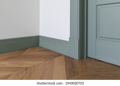 Fragment of classic interior with french herringbone parquet floor and green door and skirting boards. The final stage of finishing works in the apartment