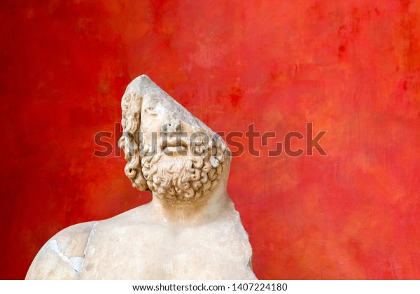 Fragment of a damaged antique sculpture against\
red background. Half a man. Incomplete or something missing\
concept. Copy space.