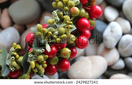 Fragment Of Decorative Chaplet In Branch Form With Colored Berries And Leaves Over Blurred Pebbles Background
