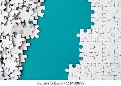 Fragment of a folded white jigsaw puzzle and a pile of uncombed puzzle elements against the background of a blue surface. Texture photo with space for text