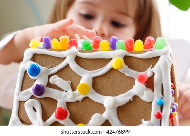 Fragment of gingerbread house roof dotted with colorful candy and little girl face on background