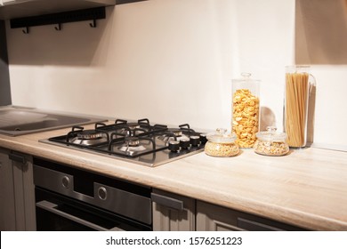 Fragment Of Home. White Kitchen. The Steel Gas Hob Detail On Beige Wooden Worktop.