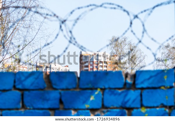 Fragment of houses and blurred the\
wall with barbed wire in the foreground. Concept of\
isolation.