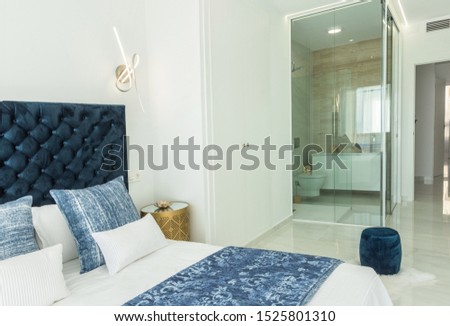 Fragment of modern bedroom in minimalist white and blue interior design style with peek a boo transparent bathroom shower enclosure combined with toilette with tempered safety glass