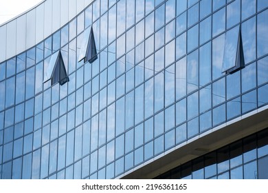 A fragment of a modern building with blue mirrored office windows that reflect the sky with clouds. Three windows are ajar. Business Center