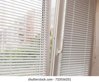 Fragment of the modern tilt and turn plastic window tilted inwards at the top with control handle and white horizontal window blinds 