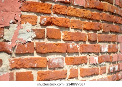 Fragment of old brickwork, close-up plan. A wall of red brick. Potholes and defects in a brick wall, side view. Flat lay, close-up. Cracks and defects in the red brick on the wall are illuminated