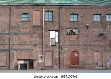 A fragment of an old and weathered facade of an old factory, made of masonry, steel and wooden frames. The old walls are cracked and the steel is corroded