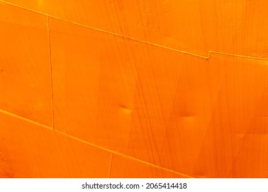 Fragment of an orange hull of industrial ship, metal sheets with weld seams, background photo texture
