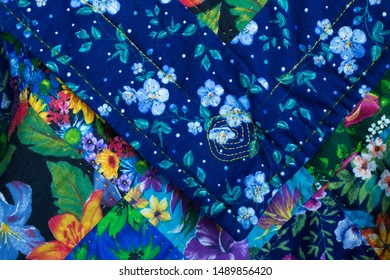 Fragment Of A Patchwork Quilt Folded In A Triangle On Top Of The Main Product In Blue With A Floral Pattern And Hand Embroidery 