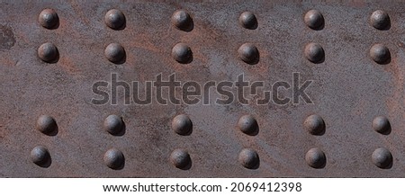 Fragment of a railroad bridge beam. Background: Rows of rivets on rusted metal.