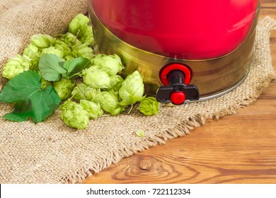 Fragment Of The Red Disposable Mini Keg Of Beer With A Built-in Beer Tap Among Of Hop Cones On Sackcloth On Wooden Surface
