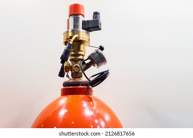 Fragment of red extinguisher. Fire extinguisher head close up. Gas fire extinguishing module with pneumatic start. Nozzle with seals on fire extinguisher cylinder. Flame control equipment.