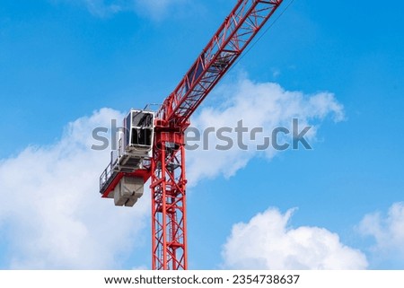 A fragment of a red tower crane with a driver's cab and a counterweight against a blue sky with light clouds.