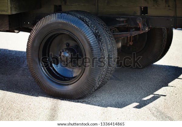 Fragment of a retro lorry\
truck with huge wheels, black tires. Oldtimer car mechanism on\
asphalt background