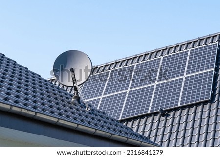 Fragment of the roof of a residential building with installed solar panels and a satellite dish. Clear blue sky.