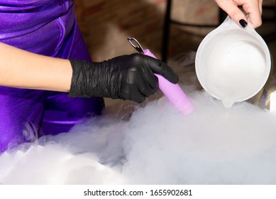 Fragment Of Scientific Show With Dry Ice. Human Hands Flowing Beverage Into Container. White Smoke, Black Gloves, Purple Costume