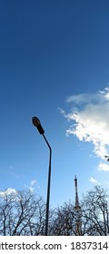 A Fragment Of A Street Lamp, The Blue Sky With White Clouds, Different Trees And Television Tower On The City Park In Autumn.