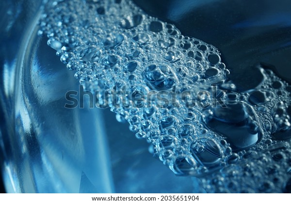 Fragment of transparent plastic bottle containing\
blue foaming liquid for glass cleaning. Windscreen washer fluid.\
The concept of modern development of chemical fluids and\
disinfectants. Macro