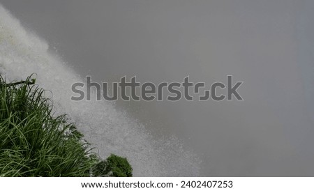 
A fragment of a waterfall. Close-up. A stream of water collapses from the slope, foaming.  Drops of water are visible in the air against a background of thick fog. Green grass in the foreground.