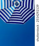 Fragment of white and blue striped beach umbrella close up against clear blue sky with text space