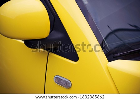 Fragment of a yellow car with a side view mirror, a windshield and a side direction indicator.