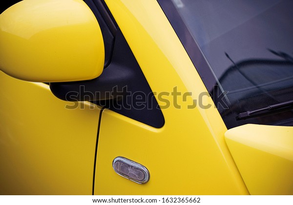 Fragment of a yellow car with a side\
view mirror, a windshield and a side direction\
indicator.