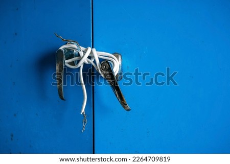 Fragments of white electric cable were tied to silver knob of steel cabinet doors. Old door locked with electric wire cable. Blue locker locked with old electric wire. Protection for safety concept.