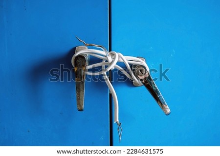 Fragments of white electric cable were tied to silver knob of steel cabinet doors. Old door locked with electric wire cable. Blue locker locked with old electric wire. Protection for safety concept.