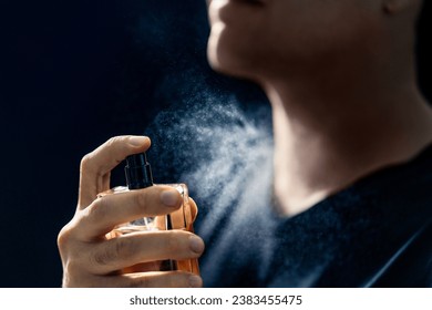 Fragrance spray. Man and perfume. Applying cologne. Scent water. Skin care, beauty product and male cosmetics concept. Holding elegant smell bottle in hand. Dark blue background. Young gentleman. - Powered by Shutterstock