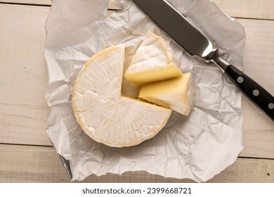 Fragrant brie cheese with paper package and knife on wooden table, macro, top view.

