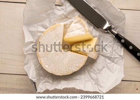 Fragrant brie cheese with paper package and knife on wooden table, macro, top view.

