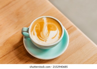 Fragrant and delicious cappuccino with beautiful foam in a blue cup on a wooden table. Beautiful concept coffee on the table. Light design for your coffee shop